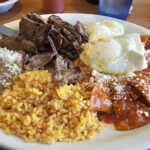 Chilaquiles rojos, with mexican rice, beans with cheese, grilled steak and two sunny side up eggs.