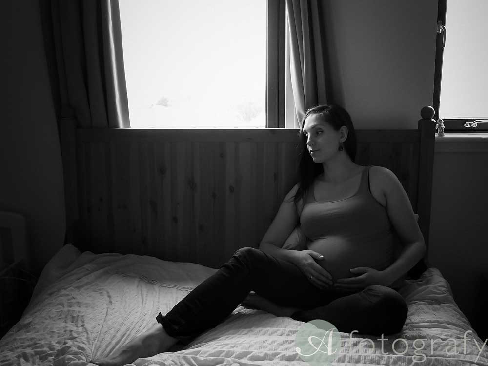 Mum to be posing on the bed during pregnancy photo shoot with soft natural lighting from the side.