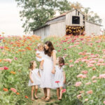 Family photographer Kelley Hoagland walking with her daughters in a flower field, showcasing her commitment to capturing family moments with clarity and precision.