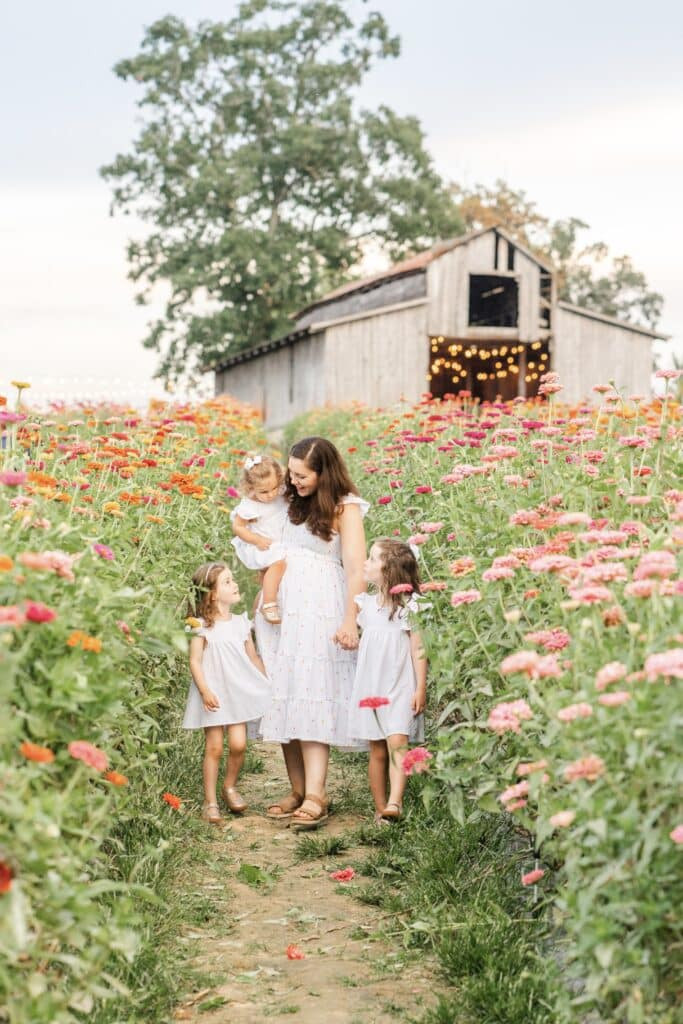 Family photographer Kelley Hoagland walking with her daughters in a flower field, showcasing her commitment to capturing family moments with clarity and precision.