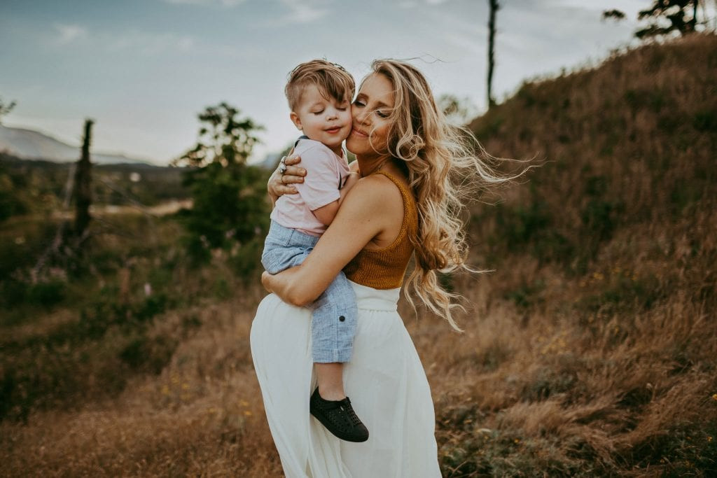 pregnant mom holding son with both eyes closed - maternity photos in portland oregon. The photo captures an intimate moment between a mother and her son, highlighting the emotional connection and anticipation of the new baby's arrival.