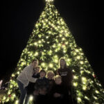 Family of three smiling in front of the Christmas tree, capturing the essence of holiday cheer