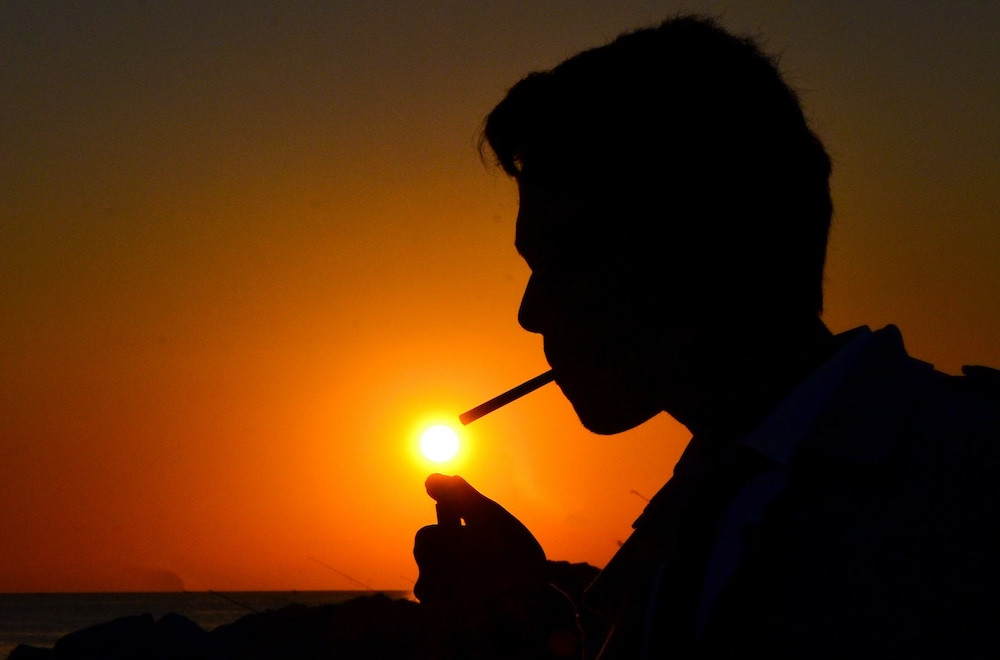 A photographer sets up a camera on a tripod with a solar filter attached to the lens, preparing to photograph the sunset over a scenic landscape.