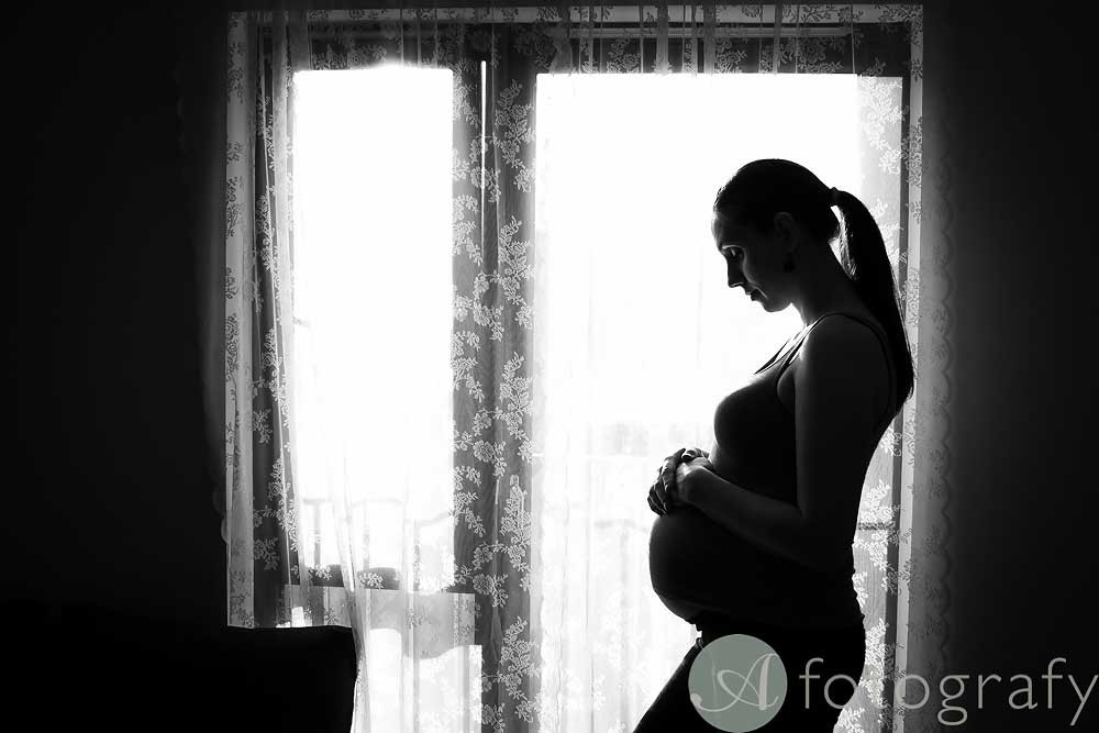 DIY home photo shoot maternity session silhouette photo against the window, capturing the outlines of the pregnant mother and partner.