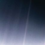 Earth appears as a tiny speck of light suspended in a sunbeam against the vastness of space.