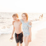 Kids smile on the beach for a photo, people are in the background; this is a post about how to edit out someone in a photo using Photoshop