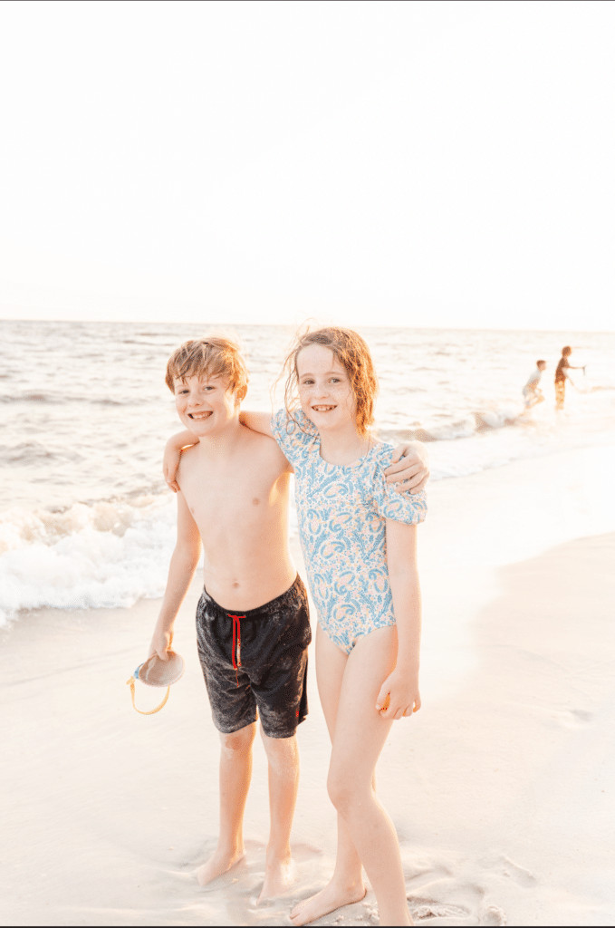 Kids smile on the beach for a photo, people are in the background; this is a post about how to edit out someone in a photo using Photoshop