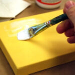 Spreading a medium layer of Mod Podge down on a canvas with a brush