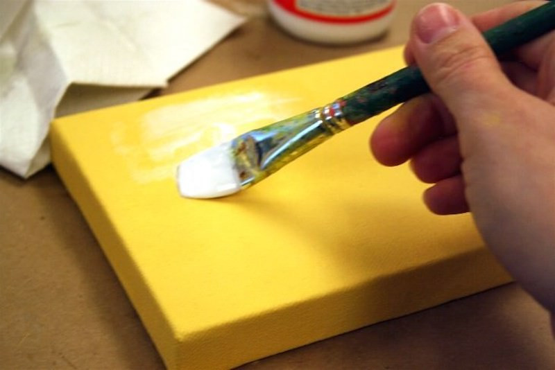Spreading a medium layer of Mod Podge down on a canvas with a brush