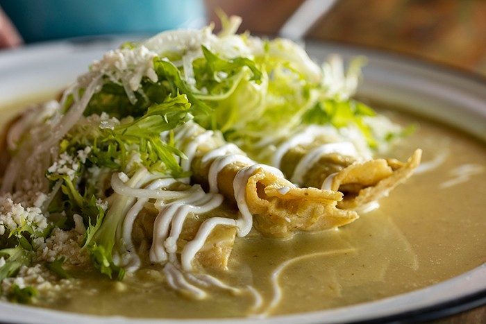 An artistic shot of A'Verde's chicken enchiladas, garnished with cotija cheese and bathed in a creamy green tomatillo sauce, enticing viewers with its rich and savory appearance.